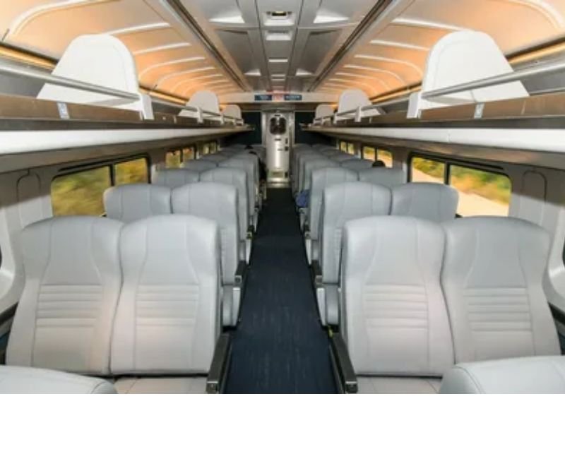 Comfortable interior of an Amtrak Coach class car with wide reclining seats and generous legroom.