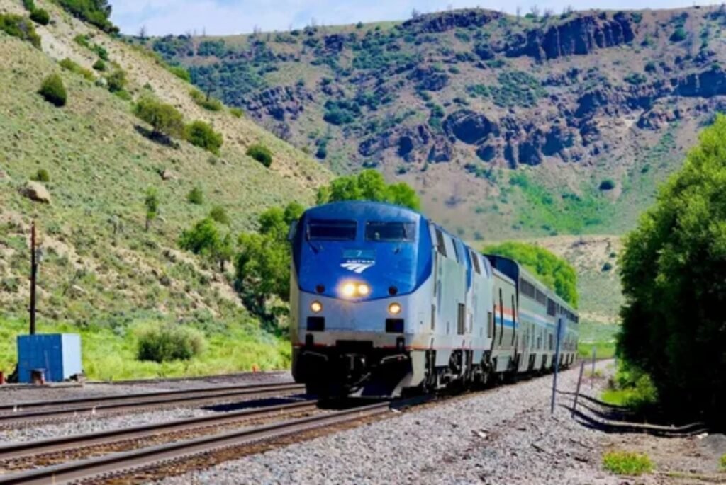 An Train ride long-distance sleeper train traveling through a scenic US mountain landscape.