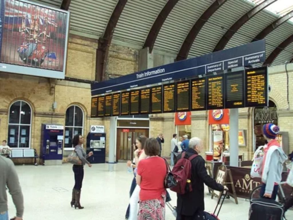 Passenger checking live train schedule departure board at railway station.