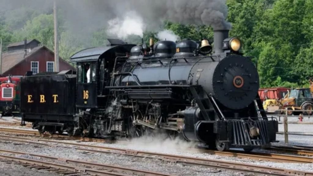 A historic steam train crossing a tall stone bridge surrounded by nature