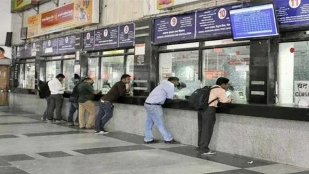 Travelers purchasing train tickets at railway station ticket counter
