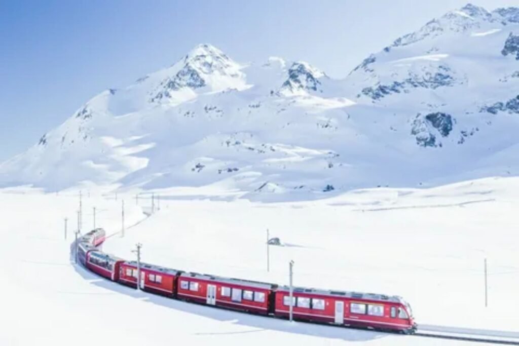 A view from inside the panoramic carriage of the Glacier Express, Switzerland, showing vast, snow-covered mountain ranges and deep valleys through the large window.