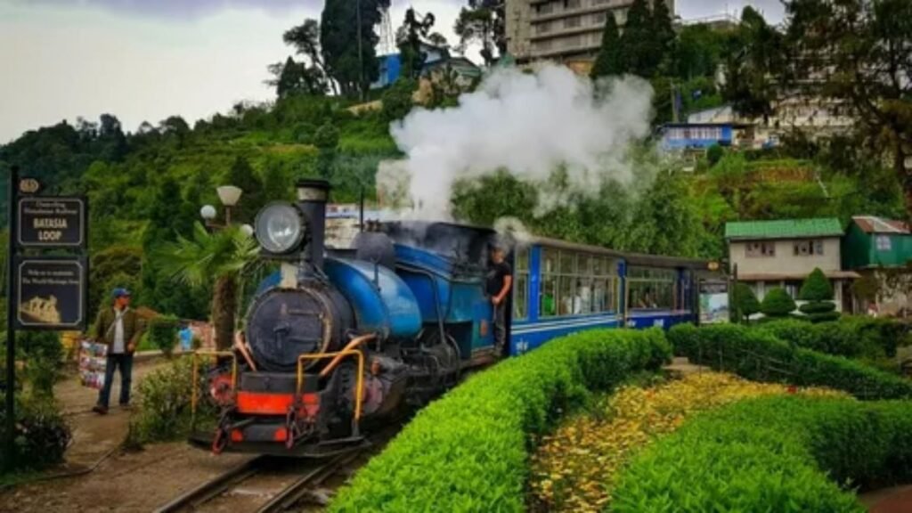 A vibrant, vintage-style photo of the Darjeeling Himalayan Railway 'Toy Train' chugging along a scenic loop through lush green hills and tea gardens in India, with high peaks under a cloudy sky.
