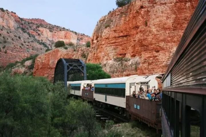 Verde Canyon Railroad train crossing a bridge surrounded by lush green valley and red rock cliffs